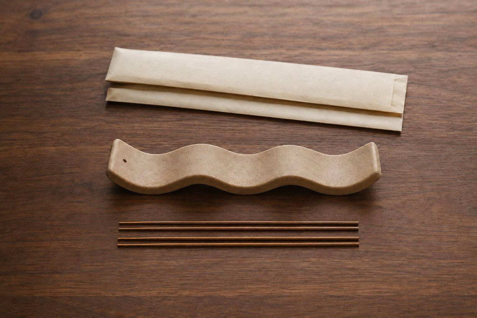 Four unlit incense sticks beside a speckled ceramic wave-shaped holder and two paper sample sleeves