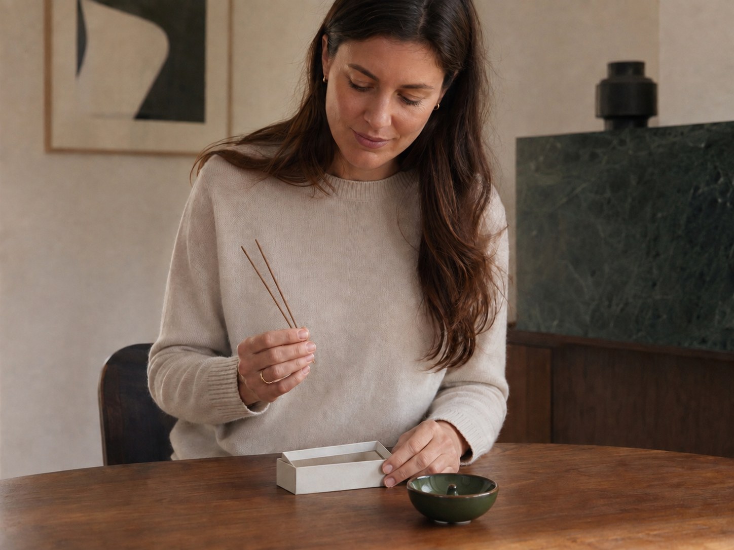 Woman comparing two straight Chinese incense sticks from a small unbranded box at a walnut dining table