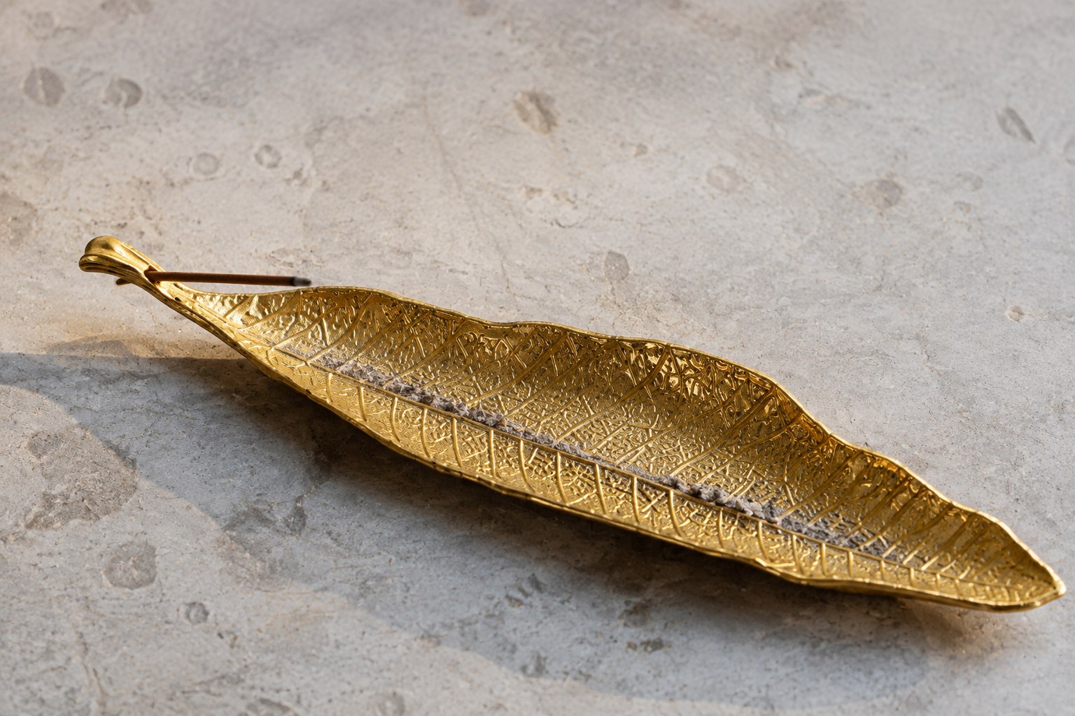 Gold leaf-shaped incense holder with a short extinguished stick and scattered ash