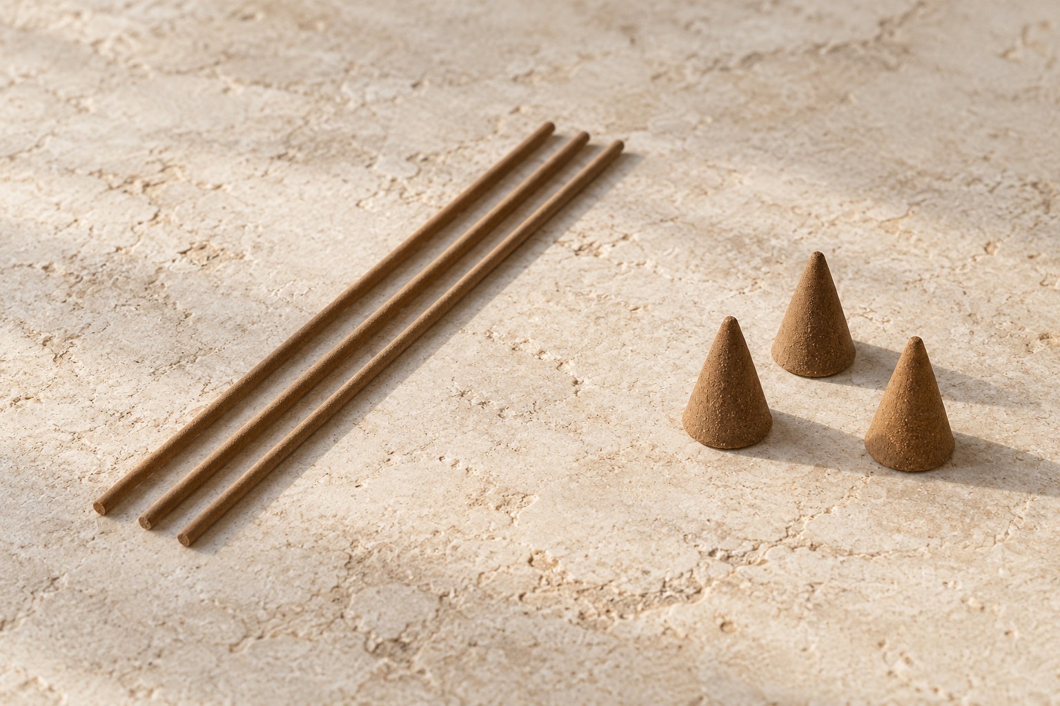 Unlit slim brown incense sticks beside small ordinary incense cones on pale stone